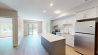 Located at 1100 Afton Drive in Windsor, Ontario, this well-designed two-bedroom, two-bathroom unit offers a clean, contemporary aesthetic throughout its thoughtfully arranged single-floor layout. Light hardwood flooring flows consistently across every room, complementing the neutral warm-grey palette that defines the interior.

The kitchen serves as the heart of the unit, featuring crisp white shaker-style cabinetry, a white tile backsplash, stainless steel appliances including a refrigerator and range, and a central island with a contrasting dark grey base and white quartz countertop — ideal for both meal preparation and casual dining.

Both bedrooms are well-proportioned, filled with natural light from large windows that frame views of the surrounding neighbourhood's mature trees and streetscape. The primary bedroom includes access to a dedicated closet outfitted with wire shelving for organized storage.

The two bathrooms maintain a consistent modern finish, with light wood-look flooring, white fixtures, and chrome hardware. The main bathroom features a wide vanity with an undermount sink, quartz countertop, white cabinetry, and a tub-shower combination.

A private balcony extends the living space outdoors, offering open views of the tree-lined neighbourhood under an open sky — a pleasant setting for relaxing or enjoying fresh air.