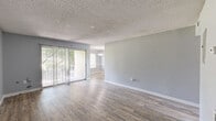 Located at 6919 Bonair Drive in Tampa, FL, this single-floor, one-bedroom, one-bathroom home offers a practical and comfortable layout. The open living and dining areas are finished with wood-look vinyl flooring and neutral gray walls, creating a clean, cohesive aesthetic throughout. A textured ceiling adds character, while sliding glass doors in the living room flood the space with natural light and provide direct access to a private patio with greenery views. The dedicated dining room features a pendant light fixture and a window overlooking the outdoors, making it a bright and inviting space for meals. The kitchen is equipped with white cabinetry, a stainless steel sink, light countertops, and a large window that brings in ample natural light. The spacious bedroom is carpeted for comfort and includes a window with outdoor views, along with access to two closets offering generous storage. The bathroom is outfitted with a full tub-shower combo with white tile surround, a granite-topped vanity, and wood-look flooring. Throughout the home, clean white baseboards and consistent gray tones create a modern, move-in ready feel.