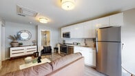 This well-designed one-bedroom, one-bathroom unit offers a thoughtful single-floor layout that maximizes functionality and comfort. The open-concept living and kitchen area serves as the heart of the space, where light wood-style flooring flows seamlessly underfoot. The kitchen is outfitted with stainless steel appliances—including a refrigerator, range, and microwave—complemented by sleek white cabinetry extending to the ceiling and a classic white subway tile backsplash. A compact dining area adjacent to the kitchen benefits from floor-to-ceiling windows that invite natural light and provide outdoor views, enhancing the sense of openness. The living area provides comfortable space for seating and relaxation, with a double-door closet offering ample storage. The bedroom is a calm, neutral retreat featuring warm wood-tone flooring, generous room for a full-sized bed and additional seating, and direct access to a closet area. The full bathroom is finished with large-format tile flooring, a combined tub and shower with glass sliding doors, a floating vanity with a backlit mirror, and clean, modern fixtures throughout. The overall ambiance is contemporary, cohesive, and light-filled.