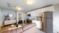 This well-designed one-bedroom, one-bathroom unit offers a thoughtful single-floor layout that maximizes functionality and comfort. The open-concept living and kitchen area serves as the heart of the space, where light wood-style flooring flows seamlessly underfoot. The kitchen is outfitted with stainless steel appliances—including a refrigerator, range, and microwave—complemented by sleek white cabinetry extending to the ceiling and a classic white subway tile backsplash. A compact dining area adjacent to the kitchen benefits from floor-to-ceiling windows that invite natural light and provide outdoor views, enhancing the sense of openness. The living area provides comfortable space for seating and relaxation, with a double-door closet offering ample storage. The bedroom is a calm, neutral retreat featuring warm wood-tone flooring, generous room for a full-sized bed and additional seating, and direct access to a closet area. The full bathroom is finished with large-format tile flooring, a combined tub and shower with glass sliding doors, a floating vanity with a backlit mirror, and clean, modern fixtures throughout. The overall ambiance is contemporary, cohesive, and light-filled.