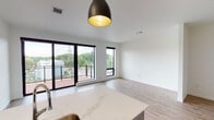 This contemporary single-floor space is thoughtfully designed with a clean, modern aesthetic throughout. The open-concept layout seamlessly connects the kitchen and living area, creating a bright and functional environment. Light wood-tone flooring flows continuously across the main living spaces, enhancing the sense of openness.

The kitchen is a standout feature, equipped with stainless steel appliances including a french door refrigerator, electric range, and microwave. White cabinetry with a subway tile backsplash pairs with a large quartz-topped peninsula that provides ample prep space and casual seating. Stylish pendant track lighting anchors the kitchen zone with a modern industrial touch.

The living area is bathed in natural light courtesy of expansive black-framed sliding glass doors and floor-to-ceiling windows that open directly onto a private balcony. The balcony offers elevated views of surrounding greenery and a waterway, providing a peaceful outdoor retreat.

The bathroom is clean and efficiently laid out, featuring a walk-in shower, a vanity with dark-toned cabinetry, and built-in storage. A hallway connects the private areas of the unit, offering a logical and practical flow. Overall, the space presents a cohesive, move-in-ready aesthetic with quality finishes throughout.