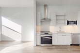 Located at 305 Winter St in Waltham, MA, this two-bedroom, one-bathroom unit offers a thoughtfully designed single-floor layout with a clean, modern aesthetic throughout. The open kitchen is a standout feature, outfitted with a full suite of stainless steel appliances including a slide-in range, built-in microwave, dishwasher, and a large refrigerator with an ice and water dispenser. Crisp white cabinetry, open shelving, a subway tile backsplash, and a stainless steel range hood complete the contemporary look, all set atop light wood-toned flooring that flows throughout the main living areas. The primary bedroom is generously proportioned and features plush carpeting, a closet with a clean panel door, and a window that allows natural light to fill the space. The second bedroom is more intimate in scale, also carpeted, with a window offering views of the surrounding neighborhood and ample sunlight. The bathroom is finished in a modern style with warm wood-tone flooring, a gray vanity with white countertop, a framed mirror with sleek overhead lighting, and a tiled walk-in shower. A connecting hallway ties the layout together efficiently. The overall ambiance is bright, clean, and move-in ready, with a consistent modern design language carried throughout every room.