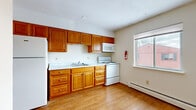 Located at 36 Court St in Geneseo, NY, this 2-bedroom, 2-bathroom unit is thoughtfully laid out on a single floor, making efficient use of its compact footprint. The kitchen is well-appointed with warm honey-toned wood cabinetry extending to the ceiling, light countertops, a double sink, and white appliances including a range, microwave, and refrigerator. Light hardwood-style flooring runs throughout the kitchen, which also features a window that brings in natural light. Baseboard heating is present throughout the unit. The primary bedroom is generously sized and features plush carpeting, a large window, and a wall-unit air conditioner, while the second bedroom is equally comfortable with carpet flooring, a closet with louvered bifold doors, and its own window. Both bedrooms offer a neutral color palette ideal for personalizing. The two bathrooms include mosaic tile flooring and white fixtures; one features a full bathtub with a window above, while the other includes a vanity with cabinet storage. Hallways connect the rooms efficiently, and louvered closet doors offer additional storage. The overall ambiance is clean and functional, suited for comfortable everyday living.