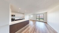 This well-designed 2-bedroom, 1-bathroom unit offers a clean, modern aesthetic across a single floor. The open-concept kitchen and living area serves as the heart of the space, featuring light hardwood flooring that extends throughout. The kitchen is outfitted with contemporary dark-wood cabinetry, crisp white upper cabinets, a sleek white countertop island with ample workspace, stainless steel appliances including a built-in microwave, wall oven, and refrigerator, plus a double sink along the back wall. Recessed lighting illuminates the space efficiently. The adjoining living area is bright and open, benefiting from a large sliding glass door and additional windows that frame outdoor views and flood the room with natural light. Both bedrooms are well-proportioned and share the same warm hardwood flooring. The primary bedroom features a sliding glass door with balcony access and a second window, offering generous natural light and outdoor views. The second bedroom includes a full-width sliding closet and a large window. Both rooms are equipped with baseboard heating. The bathroom features a full soaker tub with chrome fixtures and safety grab bars. The unit presents a clean, move-in ready interior with a bright, minimalist character throughout.