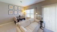 This single-floor residence offers a thoughtfully designed layout that balances comfort and functionality across its key living spaces. The combined living and dining area serves as the heart of the home, featuring neutral taupe walls, plush carpeting, and generous natural light streaming through large windows dressed with grommet-top curtains and horizontal blinds. A plush cream sofa anchors the living space, while a dark wood dining table with upholstered chairs provides an inviting area for meals. A curated gallery wall of botanical framed prints adds a refined decorative touch. The kitchen is a standout feature, showcasing dark espresso cabinetry contrasted by striking marble-effect countertops and a full suite of stainless steel appliances, including a gas range with over-the-range microwave. Rich hardwood flooring grounds the kitchen with warmth and durability. The bedroom is a serene retreat, carpeted for comfort and filled with soft natural light through a large window. A secondary room offers a versatile space currently configured as a study, complete with a glass-top desk and wall mirror. The bathroom is clean and functional, featuring a walk-in shower, a white vanity with dark countertop, built-in shelving, and tile flooring. Throughout, the space maintains a cohesive, neutral palette that creates a calm and welcoming ambiance.