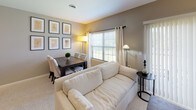 This single-floor residence offers a thoughtfully designed layout that balances comfort and functionality across its key living spaces. The combined living and dining area serves as the heart of the home, featuring neutral taupe walls, plush carpeting, and generous natural light streaming through large windows dressed with grommet-top curtains and horizontal blinds. A plush cream sofa anchors the living space, while a dark wood dining table with upholstered chairs provides an inviting area for meals. A curated gallery wall of botanical framed prints adds a refined decorative touch. The kitchen is a standout feature, showcasing dark espresso cabinetry contrasted by striking marble-effect countertops and a full suite of stainless steel appliances, including a gas range with over-the-range microwave. Rich hardwood flooring grounds the kitchen with warmth and durability. The bedroom is a serene retreat, carpeted for comfort and filled with soft natural light through a large window. A secondary room offers a versatile space currently configured as a study, complete with a glass-top desk and wall mirror. The bathroom is clean and functional, featuring a walk-in shower, a white vanity with dark countertop, built-in shelving, and tile flooring. Throughout, the space maintains a cohesive, neutral palette that creates a calm and welcoming ambiance.