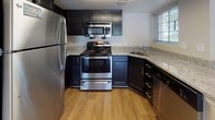 This single-floor residence offers a well-organized layout that balances open living spaces with private quarters. The living area is expansive and filled with natural light from large windows, featuring warm hardwood flooring that extends seamlessly toward the kitchen. Track lighting overhead adds a modern touch to the space.

The kitchen is thoughtfully designed with dark navy cabinetry, light granite countertops, and a full suite of stainless steel appliances, including a refrigerator, range with over-the-range microwave, and dishwasher. Wood-look flooring and a window above the sink enhance the functional yet stylish space.

Two bedrooms are finished with plush neutral carpeting and feature multiple windows that invite generous natural light and outdoor views. The clean, neutral wall tones throughout create a calm, cohesive atmosphere.

The bathroom includes a tiled tub-and-shower combination with subway-style wall tiles, a classic checkered tile floor, and a window for natural ventilation. A dedicated in-unit laundry area accommodates a stacked washer and dryer, accessed conveniently from the main hallway, adding practical value to the residence.