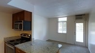 This single-floor residence offers a functional and comfortable layout centered around an open-concept living and kitchen area. The kitchen is well-appointed with granite countertops that provide ample prep and serving space, complemented by stainless steel appliances including a range and microwave. Warm-toned cabinetry adds a welcoming contrast to the light neutral walls and textured ceiling throughout the space. The kitchen flows seamlessly into the living area, creating an open and connected feel ideal for everyday living and entertaining. A window in the living area invites natural light to fill the room, offering a view of the surrounding greenery and maintaining a bright, airy ambiance. The carpeted living space provides a soft, comfortable feel underfoot, while the clean white walls and consistent finishes throughout contribute to a cohesive and tidy aesthetic. The textured ceiling adds a subtle architectural detail that carries through the space. Overall, this residence presents a practical and inviting environment with functional features and a layout designed to maximize comfort and usability.