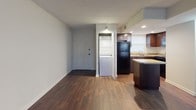 This single-floor unit is designed with a practical, open layout that maximizes the available living space. Dark hardwood-style flooring runs consistently throughout, providing a cohesive look that ties each area together. The textured ceiling adds a classic architectural detail visible across the main living spaces.

The kitchen is a functional highlight, equipped with rich dark cabinetry, a light-toned countertop, and a central island that offers additional workspace and acts as a natural divider between the kitchen and living area. A black refrigerator, double sink positioned beneath a window, and recessed lighting complete the kitchen's practical setup.

Adjacent to the kitchen, a louvered-door closet houses a stacked washer and dryer unit, providing the convenience of in-unit laundry. The main living area is generously proportioned, featuring neutral gray walls and a window fitted with blinds that allows natural light to fill the room.

A private bedroom offers a quiet retreat, with its own window for natural light and ample wall space. The full bathroom is cleanly finished with a single-sink vanity with dark hardware, a mirrored medicine cabinet, and a tiled shower-tub combination, all set against a bright, neutral palette.