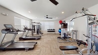 This fitness center in Clarksville, Indiana, is designed to support a comprehensive workout experience within a single-floor layout. The space features neutral-toned walls, textured carpet tile flooring, and recessed lighting complemented by ceiling fans, contributing to a clean, modern aesthetic throughout.

The cardio area is well-stocked with multiple Spirit-brand treadmills and elliptical trainers, along with stationary bikes, accommodating a range of low- and high-impact training preferences. Wall-mounted flat-screen televisions are positioned throughout the space, allowing users to stay entertained during extended sessions.

The strength and resistance training section includes a multi-station cable machine, Body-Solid branded strength equipment, adjustable benches, and a full dumbbell rack ranging across various weights. Exercise balls and additional free-weight accessories round out the functional training options.

Natural light enters through multiple windows fitted with horizontal blinds, creating a bright and inviting environment. The open floor plan ensures adequate spacing between equipment, supporting safe and comfortable movement. A mirrored door near the strength section adds depth to the space. Overall, the fitness center delivers a practical, fully equipped environment suited for a variety of fitness routines.