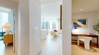 This thoughtfully designed two-bedroom, two-bathroom residence at 33 Westchester Place in New Rochelle, NY offers a refined modern living experience across a single well-appointed floor. The open-concept living, dining, and kitchen area serves as the heart of the home, anchored by a striking curved wall of floor-to-ceiling windows that floods the space with natural light and frames panoramic views of the city skyline and water beyond. Light-toned hardwood flooring runs throughout, enhancing the bright, airy atmosphere.

The kitchen is outfitted with sleek flat-panel cabinetry in warm wood tones, a clean white countertop, built-in appliances, and a marble-topped island with integrated seating — ideal for casual dining or entertaining. Pendant lighting adds a contemporary touch overhead.

The primary bedroom is a serene retreat, benefiting from large windows with expansive outdoor views, a wall-mounted split AC unit, and ample closet storage. The second bedroom is equally well-appointed with hardwood flooring and generous natural light. Both bathrooms are finished with terrazzo-style flooring, glass-enclosed showers, and modern vanities. A dedicated laundry area, a den, and five closets round out this efficiently designed and well-equipped residence.