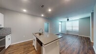 This single-story space offers a well-designed, open-concept layout with a contemporary aesthetic throughout. The kitchen serves as a focal point, featuring white shaker cabinetry, quartz countertops, a mosaic tile backsplash, and a full suite of stainless steel appliances including a refrigerator with ice maker, range, microwave, and dishwasher. A spacious center island with an undermount sink provides additional prep space and a natural gathering point that flows seamlessly into the living area. Rich, dark-toned hardwood-style flooring extends through the main living areas, complementing the neutral gray walls and recessed lighting overhead.

The living area is generously sized, fitted with a ceiling fan and windows dressed with horizontal blinds that allow for adjustable natural light. The bedrooms offer plush carpeting, ceiling fans, and sizeable windows, creating comfortable, well-lit retreats. A walk-in closet with built-in shelving and hanging rods provides ample storage. The bathrooms are finished with white cabinetry, dark-edged mirrors, and quartz-topped vanities set over wood-look flooring, delivering a clean, cohesive look throughout the entire space.