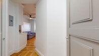 This 210 square foot studio apartment in Boston offers a thoughtful layout that maximizes every inch of space. The kitchen is the focal point, featuring crisp white cabinetry that extends to the ceiling, providing ample storage. Stainless steel appliances, including a refrigerator, oven, and over-the-range microwave, add a modern touch. A subway tile backsplash complements the clean aesthetic.

The living area, while compact, accommodates a gray sofa and benefits from natural light through a window equipped with both blinds and an air conditioning unit. Warm hardwood floors flow throughout the space, adding warmth and continuity.

The bathroom, though small, is bright and functional with a white tiled shower, chrome fixtures, and a mosaic tile floor. A hallway connects the main living area to the bathroom, likely offering additional storage solutions.

Despite its limited square footage, the apartment's layout feels open and airy, with high ceilings and a cohesive color scheme that enhances the sense of space. This studio exemplifies efficient urban living, perfect for those seeking a low-maintenance lifestyle in the heart of Boston.