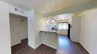 Located at 4805 Marquette NE in Albuquerque, New Mexico, this single-floor space offers a clean, modern aesthetic with thoughtful design details throughout. The kitchen is a standout feature, showcasing white cabinetry, granite-style countertops, and black appliances, including a range and refrigerator. A breakfast bar with seating overhang connects the kitchen to the adjoining living area, creating an open, sociable layout ideal for everyday living and entertaining. Elegant pendant lights hang above the kitchen, adding both style and task lighting to the space. A window above the sink and an additional window in the kitchen area allow natural light to filter in, brightening the room with views of the surrounding greenery outside. The floors are finished with rich, dark hardwood-style planks that run consistently throughout, grounding the space with warmth and cohesion. The walls are painted in a soft, neutral green tone that complements the light cabinetry and creates a calm, welcoming ambiance. Ceiling vents and well-placed lighting fixtures ensure comfort and functionality throughout. Overall, this space presents a well-maintained, move-in-ready environment with contemporary finishes in a convenient Albuquerque location.
