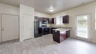 This single-story, 2-bedroom, 2-bathroom residence in Layton, Utah offers a practical and cohesive layout designed for comfortable everyday living. The kitchen is a standout feature, equipped with rich dark-espresso cabinetry, granite-look countertops, black appliances including a range, microwave, and refrigerator, and a double-basin sink beneath a window that lets in natural light. Light wood-look flooring runs throughout the main living and kitchen areas, lending a clean, modern aesthetic. The open living area provides a generous, versatile space with neutral wall tones and flush-mount ceiling lighting. Both bedrooms are carpeted and feature large windows with blinds that allow ample natural light, creating a bright and restful atmosphere. The primary bedroom includes a spacious walk-in closet with built-in shelving and hanging rods for organized storage. Both bathrooms mirror each other in design, each offering dark wood vanities with granite-look countertops, a single sink, a full tub-shower combination, and light wood-look tile flooring. A dedicated in-unit laundry room with side-by-side washer and dryer connections and overhead shelving adds convenience. The overall design is neutral, clean, and functional throughout.