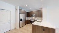 Located at 1997 S Acoma St in Denver, Colorado, this single-floor unit showcases a clean, contemporary design with consistent light wood flooring and a neutral color palette throughout. The open-concept kitchen is a standout feature, outfitted with flat-front dark walnut cabinetry extending to the ceiling, a subway tile backsplash, stainless steel appliances including a French door refrigerator and range, and a peninsula with a white quartz countertop and undermount sink — ideal for both cooking and casual dining.

The living area flows naturally from the kitchen, offering an open, airy feel with recessed lighting overhead. A built-in niche with integrated shelving and a desk area provides a practical workspace or display space near the entry. The living space connects to a private balcony through large sliding glass doors, offering elevated views of the surrounding Denver neighborhood and bringing in generous natural light.

The bathroom is well-appointed with a dark wood floating vanity, white quartz countertop, large-format tile flooring, and a soaking tub framed by marble-style tile surround. Additional rooms feature sliding glass door access to a shared balcony and ample wall space, each benefiting from natural light and the same cohesive finishes found throughout the unit.