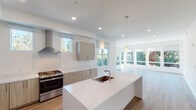 This single-floor residence showcases a clean, contemporary design highlighted by crisp white walls, wood-look plank flooring, and an abundance of natural light throughout. The open-concept kitchen serves as a central focal point, featuring light wood-grain cabinetry, quartz countertops with subtle veining, a large waterfall-edge island with an undermount sink, stainless steel appliances including a gas range and refrigerator, and a sleek wall-mounted range hood. Pendant lighting and recessed fixtures illuminate the space, which flows seamlessly into a bright, spacious living area lined with expansive floor-to-ceiling windows and a glass door leading to a balcony with views of surrounding trees and neighboring rooftops.

The bedrooms are well-proportioned, each featuring wood-look flooring, neutral walls, and windows that allow natural light and outdoor views. The en suite bathroom is finished with a dual-sink vanity featuring light wood cabinetry and white quartz countertops, a large wall mirror with vanity lighting, a glass-enclosed walk-in shower with tile surround, and a separate water closet. A hallway with a sliding-door closet connects additional rooms. Throughout the unit, consistent use of neutral tones and modern finishes creates a cohesive, polished ambiance.