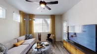 This well-appointed single-floor residence offers a thoughtfully designed layout that balances comfort and modern style. The living room serves as the heart of the home, featuring wood-look plank flooring, a ceiling fan with integrated lighting, and large windows dressed with bold yellow patterned curtains that allow ample natural light to fill the space. A wall-mounted flat-screen TV and a media console complement the relaxed seating arrangement, creating an inviting atmosphere for everyday living.

The kitchen is outfitted with white shaker-style cabinetry, gray quartz-style countertops, a tile backsplash, and a full suite of stainless steel appliances including a refrigerator, electric range, and over-the-range microwave. A window above the sink brings in natural light, enhancing the clean, functional workspace.

Adjacent to the kitchen, the dining area features wood-look flooring, a round dining table with seating, and a breakfast bar with countertop seating — ideal for both casual meals and entertaining. A large decorative mirror and framed artwork add character to the space.

The bedroom is a peaceful retreat with plush carpeting, a ceiling fan, a window with natural light, and ample room for furnishings. The full bathroom features a combined tub and shower, a single-sink vanity with gray countertops, white cabinetry, and wood-look flooring, delivering a clean and modern aesthetic throughout.