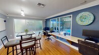 Located at 475 Appleyard Drive in Tallahassee, Florida, this single-floor leasing office for The Landing at Tallahassee is a professionally designed workspace that balances functionality with a welcoming atmosphere. The interior is finished with warm hardwood flooring throughout and elegant crown molding, complemented by a two-tone color scheme of cool slate blue and bold navy accent walls that lend the space a polished, contemporary character.

The main workspace features a long built-in countertop workstation that runs along the wall, equipped with desktop computers, a printer, and ample surface area to accommodate staff and residents alike. Large sliding glass doors and wide windows along the exterior wall provide clear views of the outdoor pool area, flooding the space with natural light. A glass-top high-bar table with bar-height chairs serves as a casual meeting or consultation area at the center of the room.

Additional functional elements include a whiteboard, a cork bulletin board displaying community information and notices, and track lighting that ensures the space is well-illuminated. A set of glass French doors connects this office to an adjoining common area, promoting an open and accessible environment. The frosted glass windows prominently feature The Landing's branding logo, reinforcing the community's identity throughout the space. Overall, the office presents a clean, organized, and welcoming setting for leasing inquiries and resident services.