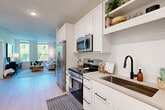 Located at 110 E 36th Street in Charlotte, NC, this well-appointed one-bedroom, one-bathroom residence offers a thoughtfully designed layout with modern finishes throughout. The open floor plan connects the kitchen and living area seamlessly, creating a sense of spaciousness and easy flow.

The kitchen is a standout feature, outfitted with crisp white shaker-style cabinetry, open shelving, a white subway tile backsplash, stainless steel appliances including a range, over-the-range microwave, refrigerator, and dishwasher, plus a matte black pull-down faucet over a single-basin sink with stone-toned countertops. Light wood-style flooring runs throughout the main living areas, enhancing the bright, airy atmosphere.

The living area benefits from large windows that invite abundant natural light and offer views of surrounding greenery. The bedroom is a calm, comfortable retreat with a dedicated window framing treetop views, carpet flooring, and a dedicated closet for storage.

The bathroom features a long, floating vanity with dual mirrors framed in black, stone-topped counters, matte black fixtures, and a shower-tub combination. Clean white walls and light flooring maintain a cohesive, modern aesthetic throughout the space.