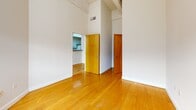 Located at 1418 W Marshall St in Richmond, VA, this 2-bedroom, 2-bathroom unit offers a compelling blend of industrial character and practical living across a single floor. The space is immediately distinguished by its exposed brick walls, which appear throughout multiple rooms, adding warmth and historic texture to the interior. Warm-toned hardwood flooring runs through the main living areas and bedrooms, complementing the raw architectural details. Soaring ceilings — accented by white-painted wooden beams — create a sense of openness well beyond the unit's compact footprint. The kitchen features a peninsula-style breakfast bar and white cabinetry with dark countertops, opening toward the main living area through a structural column that adds to the loft-like aesthetic. Natural light enters through large windows fitted with vertical blinds in both bedrooms, each of which showcases exposed brick accent walls. The primary bedroom offers generous proportions with dual wooden doors providing access to closets and the hallway. Both bathrooms are tiled and include vanities with under-sink storage and wall-mounted medicine cabinets; one bathroom features a tub-shower combo, while the other highlights a brick accent wall with a bright window. A utility room and hallway complete the layout, ensuring efficient use of every square foot.
