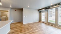 Located at 5053 Shelby Ave in Rapid City, South Dakota, this single-floor residence offers two bedrooms and two bathrooms within a efficiently designed layout. The open-concept kitchen and living area serves as the heart of the home, featuring warm light vinyl plank flooring, gray cabinetry with light countertops, and a full suite of black appliances including a refrigerator, electric range, and over-the-range microwave. A pendant light and recessed lighting illuminate the kitchen, while the adjacent living area benefits from a glass exterior door that invites natural light and outdoor views. Exposed ductwork adds an industrial accent throughout the common areas. Both bedrooms are finished with neutral-toned carpet and windows that bring in natural light, providing comfortable, restful spaces. The primary bedroom includes dedicated closet space. The two bathrooms are finished with tile flooring and wood-toned cabinetry; one features a walk-in shower stall, while the other includes a soaking tub and vanity with mirror. The overall palette of soft grays and warm neutrals creates a clean, cohesive aesthetic throughout the home, making it a practical and comfortable residence in Rapid City.
