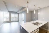 Located in Edmonton's vibrant Oliver neighbourhood, this modern 2-bedroom, 2-bathroom high-rise unit offers a well-designed open-concept layout with upscale finishes throughout. Light hardwood flooring flows consistently across the living areas, complemented by neutral grey and taupe tones that create a clean, contemporary atmosphere.

The kitchen serves as a central focal point, featuring a large waterfall-edge quartz island with an undermount sink, sleek dark wood cabinetry, white upper cabinets, stainless steel appliances, and elegant pendant lighting overhead. Both bathrooms are finished with marble-look porcelain tile floors, quartz countertops, dark wood vanities, and large mirrors, with one featuring a full soaker tub and shower combination.

The two bedrooms are bright and well-proportioned, with floor-to-ceiling windows drawing in abundant natural light and showcasing sweeping panoramic views of the Edmonton skyline. The primary bedroom includes a closet and direct access to a full ensuite bathroom. A private balcony with glass railings extends the living space outdoors, offering unobstructed elevated views of the city and surrounding neighbourhoods — a standout feature of this high-rise residence.