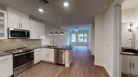 Located at 2727 Live Oak in Dallas, TX 75204, this single-floor residence offers a thoughtfully designed open-concept layout that seamlessly connects the kitchen, dining, and living areas. The kitchen is a standout feature, showcasing white shaker cabinetry, dark granite countertops, a herringbone tile backsplash, and a full suite of stainless steel appliances including a French door refrigerator, range, microwave, dishwasher, and a built-in beverage cooler. A peninsula with pendant lighting and a gold-toned faucet adds both style and functionality. Warm hardwood-style flooring runs throughout the main living spaces, lending continuity and a welcoming feel. The living area is bright and airy, benefiting from large windows that invite natural light and offer views of the surrounding neighborhood. A ceiling fan provides comfort and a relaxed ambiance. The bathroom is particularly distinctive, featuring bold black-and-white patterned encaustic-style tile flooring, a dual-sink vanity with dark countertops, and a separate shower and soaking tub area. Clean white walls and recessed lighting throughout the unit contribute to a crisp, modern aesthetic. Overall, the space delivers a refined urban living experience in the heart of Dallas.