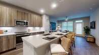 This thoughtfully designed single-floor residence offers a seamless blend of modern aesthetics and functional living. The open-concept layout connects the kitchen, dining, and living areas, creating a welcoming and cohesive space filled with natural light from large windows. The kitchen is a standout, featuring warm wood-tone cabinetry extending to the ceiling, stainless steel appliances, a classic subway tile backsplash, and a generous quartz-topped island with built-in sink — ideal for both meal preparation and casual dining with wicker bar seating. The living area is bright and inviting, anchored by hardwood-style flooring, a wall-mounted television, and a private entrance door flanked by expansive windows that draw in abundant natural light. Two spacious bedrooms offer plush carpeting, ceiling fans, and generous natural light through well-dressed windows. The bathroom is elegantly finished with wood-framed mirrors, quartz countertops, tile flooring, and a tub-shower combination, complemented by an adjacent walk-in closet with built-in shelving. Throughout the residence, neutral tones and clean lines create a calm, contemporary ambiance suited for comfortable everyday living.