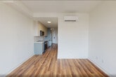 Located at 873 Communipaw Avenue in Jersey City, NJ, this thoughtfully designed studio unit makes efficient use of its single-floor layout. The open-plan kitchen and living area forms the heart of the space, featuring warm hardwood-style flooring that runs throughout and crisp white walls that create a bright, clean aesthetic. The kitchen is equipped with stainless steel appliances, including a microwave, range, and refrigerator, alongside contemporary gray cabinetry and a functional countertop workspace. A wall-mounted mini-split system provides climate control directly within the living area. Natural light fills the living space through a large, modern picture window with a black frame, offering open views of the surrounding Jersey City neighborhood. The bathroom is finished with light tile flooring and includes a soaking tub, toilet, and chrome hardware accents, maintaining the unit's clean, neutral palette. A dedicated closet provides storage, while a laundry area houses a stacked washer and dryer unit tucked neatly behind a full-height door, adding everyday convenience. The overall ambiance is modern and minimalist, with consistent finishes throughout that create a cohesive and functional living environment.