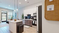 Located at 877 Lavina St in Fort Wayne, Indiana, this thoughtfully designed one-bedroom, one-bathroom residence offers a modern aesthetic with high-quality finishes throughout. The open-concept layout connects the kitchen, dining area, and living room, creating a cohesive and functional living space.

The kitchen is a standout feature, boasting white upper cabinetry paired with dark lower cabinets, a bold dark tile backsplash, white quartz countertops, and a full suite of stainless steel appliances including a refrigerator, range, microwave, and dishwasher. A central island provides additional prep and casual dining space.

The living room is bathed in natural light through large, grid-paned windows and a glass-paneled entry door that frames views of the neighborhood. Elevated ceilings enhance the sense of openness throughout the main living area.

The bedroom is a well-proportioned retreat featuring plush carpeting, a large grid-style window with outdoor views, and ample wall space. A dedicated closet provides convenient storage.

The bathroom features a sleek, modern vanity with dark wood cabinetry, white quartz countertops, matte black fixtures, a large rectangular mirror, and stylish hexagonal tile flooring. Light wood-style flooring flows throughout the main living areas, completing the contemporary design.