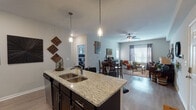 Located in Clarksville, Tennessee, this single-story residence offers a thoughtfully designed open-concept floor plan that seamlessly connects the kitchen, dining, and living areas. The kitchen is a standout feature, showcasing dark espresso cabinetry, granite countertops, stainless steel appliances including a French door refrigerator, a subway tile backsplash, and a central island with bar seating illuminated by pendant lighting — ideal for both meal prep and casual dining. Wood-style flooring flows throughout the main living areas, adding warmth and continuity to the space. The dining area transitions naturally into the living room, which is bright and welcoming, featuring large windows dressed with grommet-style curtains that allow generous natural light. A ceiling fan adds comfort to the living space. The bedrooms are carpeted for coziness and include windows with blinds and curtains, as well as ceiling fans in select rooms. The bathroom continues the granite and dark cabinetry aesthetic seen in the kitchen, with a shower-tub combination and ample vanity space. A dedicated laundry area with washer and dryer is also included. Overall, this residence presents a cohesive, modern aesthetic with functional, well-finished spaces throughout.