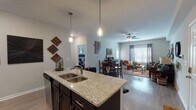Located in Clarksville, Tennessee, this single-story residence offers a thoughtfully designed open-concept floor plan that seamlessly connects the kitchen, dining, and living areas. The kitchen is a standout feature, showcasing dark espresso cabinetry, granite countertops, stainless steel appliances including a French door refrigerator, a subway tile backsplash, and a central island with bar seating illuminated by pendant lighting — ideal for both meal prep and casual dining. Wood-style flooring flows throughout the main living areas, adding warmth and continuity to the space. The dining area transitions naturally into the living room, which is bright and welcoming, featuring large windows dressed with grommet-style curtains that allow generous natural light. A ceiling fan adds comfort to the living space. The bedrooms are carpeted for coziness and include windows with blinds and curtains, as well as ceiling fans in select rooms. The bathroom continues the granite and dark cabinetry aesthetic seen in the kitchen, with a shower-tub combination and ample vanity space. A dedicated laundry area with washer and dryer is also included. Overall, this residence presents a cohesive, modern aesthetic with functional, well-finished spaces throughout.