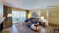 Located at N Wind Place in Charlotte, NC, this single-floor residence offers a thoughtfully designed layout that balances comfort and functionality. The living room serves as the heart of the home, highlighted by a classic brick fireplace and large sliding glass doors fitted with vertical blinds that open to an outdoor balcony, flooding the space with natural light and providing views of the surrounding area. Warm wood-style flooring runs throughout the main living spaces, complementing the neutral wall tones.

The galley-style kitchen is efficiently arranged with white cabinetry, gray countertops, black appliances including a range, microwave, and refrigerator, and a stainless steel sink. Track lighting overhead brightens the workspace. Adjacent to the kitchen, the dedicated dining area features a pendant light fixture and a bold navy accent wall that adds a striking visual contrast to the otherwise warm, neutral palette.

The bedroom is a restful retreat with plush carpeting, large windows dressed in gray drape panels, and ample space for furnishings. The full bathroom includes a tub-shower combination, a vanity with storage, and wood-style flooring. Throughout the residence, consistent design choices — warm tones, modern fixtures, and curated décor — create a cohesive and inviting ambiance.