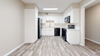 Located at 7200 Eby Dr in Merriam, Kansas, this single-floor, 2-bedroom, 1-bathroom unit offers a practical and well-appointed layout with a clean, neutral aesthetic throughout. The living area is bright and open, featuring plush carpeting, soft gray walls, and multiple windows that invite natural light and outdoor views. A glass-paned door provides additional brightness and direct access to the exterior. The kitchen is a standout feature, showcasing white shaker-style cabinetry, light stone countertops, a classic subway tile backsplash, and wood-look vinyl plank flooring. Black appliances — including a refrigerator, electric range, dishwasher, and over-range microwave — provide a striking contrast against the white cabinetry. A skylight-style overhead fixture keeps the space well-lit. The spacious primary bedroom offers generous closet space with two sets of bifold closet doors, soft carpeting, and a ceiling fan with light. The second bedroom is also carpeted, features ceiling fan lighting, and benefits from multiple windows. The bathroom is clean and bright, with a tiled tub-shower combination and wood-look flooring. Hallways connect the rooms efficiently, contributing to the unit's functional flow.