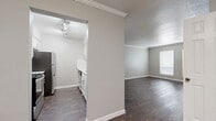 Located at 7350 Brompton Rd in Houston's 77025 corridor, this single-floor residence offers two bedrooms, two bathrooms, and two closets within a well-organized layout. The living area features rich dark hardwood-style flooring, crown molding, a textured ceiling, and dual windows that welcome natural light, creating a bright and welcoming atmosphere. The adjacent kitchen is semi-open, separated by a partial wall, and is equipped with white cabinetry, a stainless steel refrigerator, and track lighting overhead. Both bedrooms are carpeted for comfort and include ceiling fans with integrated lighting. The generously sized primary bedroom features a window for natural light and access to a dedicated closet with built-in shelving. The second bedroom is similarly appointed with its own closet. Each bathroom is finished with dark hardwood-style flooring, white vanities topped with light quartz-style countertops, and a tub/shower combination surrounded by large-format, light-toned tile. The neutral gray color palette throughout the home lends a cohesive and contemporary aesthetic. Mature trees visible from the exterior provide a touch of greenery to the surroundings.