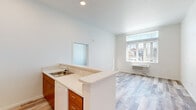 Located in Beaverton, Oregon, this single-floor residence offers four bedrooms and two full bathrooms within a thoughtfully designed layout. The open-concept kitchen is a standout feature, equipped with warm-toned wood cabinetry, white quartz countertops, a peninsula with a built-in sink, a full suite of white appliances including a refrigerator and range, and recessed lighting overhead. Light wood-look flooring flows through the kitchen and living areas, creating a cohesive and airy feel. Large windows with vertical blinds flood the living space with natural light and offer views of the surrounding neighborhood. The bedrooms are carpeted with a durable, neutral-toned carpet and include generous closet space with sliding doors. Each room benefits from natural light through sizable windows. Both bathrooms feature a consistent design language, with wood-toned vanities, white quartz countertops, and full tub-shower combinations equipped with curved rods and accessible grab bars. The clean white walls and high ceilings throughout contribute to a bright, open ambiance. Each room's wall-mounted HVAC unit ensures individual climate comfort. This well-appointed home presents a modern, move-in-ready environment suited for a range of occupants.