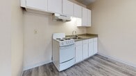 This 1-bedroom, 1-bathroom apartment offers a functional and efficient single-floor layout designed to maximize its compact footprint. The living area features grey wood-style laminate flooring, warm neutral-toned walls, and a textured ceiling. A large window with vertical blinds allows natural light to fill the space, while a wall-mounted air conditioning unit and baseboard heater provide year-round climate control. A ceiling fan adds additional comfort to the main living area.

The kitchen is open to the living space and is equipped with white cabinetry, a granite-style countertop, a white electric range with coil burners, an under-cabinet range hood, and a single-basin sink. The layout is straightforward and practical for everyday use.

The bedroom features plush carpet flooring and includes a reach-in closet with a full-length hanging rod, offering convenient storage. The bathroom is clean and bright, with a white vanity, mirrored medicine cabinet, a tub-shower combination, and wood-style flooring that ties back to the rest of the unit.

A closet near the entry provides additional storage. Overall, the apartment presents a clean, no-frills living space with consistent finishes and a practical design suited for comfortable everyday living.