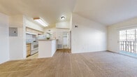 Located at 700 W Belleview Ave in Littleton, Colorado, this one-bedroom, one-bathroom residence offers a well-organized single-floor layout designed for comfortable everyday living. The living room serves as the heart of the home, highlighted by soaring vaulted ceilings that lend an open, airy feel. A tile-surround fireplace anchors the room, while a sliding glass door provides direct access to a private balcony, filling the space with natural light. Plush carpeting extends throughout the living areas and bedroom, adding warmth underfoot. The galley-style kitchen features a breakfast bar peninsula, light wood cabinetry, a skylight, tile flooring, a double-basin sink, and white appliances. A chandelier overhead adds a touch of elegance. The bedroom is a comfortable retreat with vaulted ceilings, a large window framing outdoor views, and a reach-in closet with built-in shelving. The bathroom includes a single vanity with ample mirror space and a multi-bulb light fixture. A dedicated laundry room with overhead cabinetry, tile flooring, and washer hookups adds everyday convenience. This thoughtfully laid-out residence combines functional design with charming architectural details throughout.