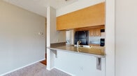 Located at 13500 Rodgers Ave in Largo, Florida, this single-floor residence offers a straightforward and functional layout designed for comfortable everyday living. The open-concept kitchen is a central feature, equipped with wood-tone cabinetry, a black refrigerator, an electric range, and a granite-style countertop that extends into a pass-through breakfast bar — ideal for casual dining or additional prep space. The kitchen floor is finished in warm hardwood-style flooring, and a built-in pantry with wire shelving provides convenient storage. The living area is generously sized, finished with neutral wall-to-wall carpeting and a ceiling fan overhead, creating a comfortable and airy atmosphere. A private entry door opens directly into this space. The bedroom offers a calm retreat, carpeted and bathed in natural light through large windows fitted with vertical blinds. A second carpeted room with sliding glass doors and vertical blinds provides outdoor access and additional natural light. The bathroom includes a full tub-shower combination with clean white tile surround. Textured ceilings are consistent throughout the home, complementing the neutral color palette that ties the entire space together cohesively.