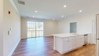 This well-appointed single-floor residence offers a thoughtfully designed open-concept layout that seamlessly connects the kitchen and living area. The kitchen is a standout feature, showcasing tall white shaker-style cabinetry, gleaming quartz countertops, a large center island with an undermount sink, and a full suite of stainless steel appliances including a gas range, built-in microwave, and refrigerator. Light hardwood-style flooring flows throughout the main living areas, complemented by recessed lighting and classic crown molding that adds a refined architectural touch. The living area is generously sized and filled with natural light, with large sliding glass doors opening onto a private balcony overlooking a green outdoor setting. The bedrooms are carpeted for comfort and feature neutral tones, ample space, and walk-in closets with built-in shelving. The bathroom includes a full soaking tub and shower combination with clean white subway tile surround and chrome fixtures. Throughout the space, a consistent palette of soft whites and warm neutrals creates a bright, clean, and welcoming ambiance suited for everyday living.