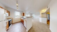 Located at 10115 Jeffreys St in Las Vegas, NV, this 2-bedroom, 2-bathroom residence offers a thoughtfully designed single-floor layout with a bright, open feel throughout. The heart of the home is a combined dining, kitchen, and living area where warm wood-toned cabinetry, a peninsula with a breakfast bar overhang, and a full suite of white appliances — including a refrigerator, gas range, microwave, and dishwasher — define the kitchen. Wood-style flooring runs through the kitchen and dining space, while plush carpeting extends into the living area and bedrooms. Track lighting illuminates the main living spaces, and multiple windows invite generous natural light. The living area leads to a private balcony via a glass-paneled door. The primary bedroom is a comfortable size, featuring a distinctive bay window arrangement that frames outdoor greenery views, along with soft carpet flooring. The second bedroom also offers carpeting and ample wall space. Both bathrooms are clean and functional, with one featuring a tub/shower combo, wood-style flooring, and a large vanity mirror. A dedicated in-unit laundry room accommodates a full-size washer and dryer with built-in shelving above. Two closets and a hallway complete this well-organized and move-in-ready Las Vegas residence.