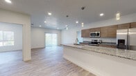 This well-designed single-floor unit offers a clean, contemporary aesthetic throughout. The open-concept layout connects the kitchen and living area seamlessly, creating a bright and airy atmosphere enhanced by recessed lighting and elegant pendant fixtures. The kitchen is a standout feature, equipped with stainless steel appliances including a range, microwave, and French door refrigerator, complemented by warm wood-toned cabinetry and granite countertops that extend across a generous island with a built-in sink. Light wood-look flooring runs consistently throughout the unit, adding warmth and visual continuity. The living area benefits from natural light via a sliding glass door fitted with vertical blinds, while the entryway provides a clean, welcoming transition into the space. The bedrooms are well-proportioned and bright, with large windows framing views of surrounding greenery and distant mountain ridgelines. The bathrooms are finished with granite-topped wood vanities, brushed gold fixtures, and clean white tile, with one bathroom offering a walk-in shower and another featuring a tub-shower combination. The overall ambiance is modern, neutral, and move-in ready, with consistent finishes that lend a cohesive and polished feel throughout.