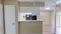 This two-story residence offers a practical and well-organized layout across two distinct floors. The main level encompasses the living and functional areas, featuring durable wood-look flooring throughout. The open-concept kitchen is equipped with black appliances, including a refrigerator, gas range, and over-the-range microwave, complemented by white cabinetry and a speckled countertop peninsula that separates the kitchen from the living area. The living room receives natural light through a window fitted with blinds, creating a bright and welcoming atmosphere. A full bathroom on this level includes a tiled tub-shower combination, a vanity with a speckled countertop, and wood-look flooring. A staircase with metal railings connects the two floors. The upper level is dedicated to the spacious primary bedroom, which is carpeted and features a ceiling fan with a light fixture, a window allowing in natural light, and a large built-in sliding-door closet with shelving. A second bathroom on this floor provides a vanity with a single-basin sink, a mirror, and a towel bar. Throughout the space, neutral warm-beige wall tones and textured ceilings contribute to a cohesive and understated aesthetic.