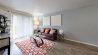 This single-floor residence offers a thoughtfully designed layout that balances comfort and functionality across its key living spaces. The living room serves as the heart of the home, featuring wood-look flooring, neutral gray walls, and a large sliding glass door dressed with vertical blinds that fill the room with natural light and provide access to the outdoors. The open, airy feel is enhanced by clean lines and a welcoming ambiance.

The kitchen is efficiently arranged with crisp white cabinetry, white appliances including a refrigerator, range, and dishwasher, and wood-look flooring that flows seamlessly from the living area. The layout maximizes counter and storage space, making it a practical workspace for daily use.

The bedroom is a serene retreat, carpeted for warmth and comfort, with a large window dressed in teal curtains that invite natural light. The room includes generous space for a full furniture arrangement and connects directly to the bathroom, offering convenient ensuite-style access. A walk-in closet provides ample storage.

The bathroom features wood-look flooring, a wide vanity with cream cabinetry, a large mirror, and bright overhead lighting, lending a clean and polished finish. Throughout the residence, a cohesive warm-neutral color palette and consistent flooring choices create a unified and inviting atmosphere.