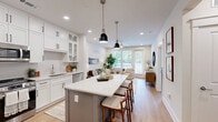 Located on Statesville Road in Huntersville, NC, this thoughtfully designed one-bedroom, two-bathroom residence combines modern aesthetics with practical functionality across a single, efficiently organized floor.

The open-concept kitchen and living area serves as the heart of the home. The kitchen is outfitted with floor-to-ceiling white shaker cabinetry accented by matte black hardware, stainless steel appliances, quartz countertops, an undermount sink, and a central island with seating — ideal for both meal prep and casual dining. Light wood-tone flooring and recessed lighting carry throughout, creating a warm, cohesive atmosphere.

The adjacent living room is bright and welcoming, featuring large windows with outdoor views and a ceiling fan overhead. The spacious primary bedroom includes ample natural light from oversized windows, a ceiling fan, and direct access to a walk-in closet with built-in shelving.

Both bathrooms are finished to a high standard. The primary bath features large-format tile in a walk-in glass-enclosed shower with a built-in bench, while the second bath includes a white vanity with quartz countertops and decorative tile flooring. Additional highlights include a dedicated laundry area, a functional entryway nook, and consistent light-toned finishes throughout that contribute to a clean, modern ambiance.