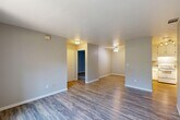 Located at 4146 Madison Ave in North Highlands, California, this single-story 2-bedroom, 1-bathroom home offers a practical and comfortable layout with consistent wood-look flooring carried throughout every room. The open living area is bright and welcoming, featuring a ceiling fan and a neutral gray color palette that creates a clean, modern feel. The combined kitchen and living room space connects seamlessly, with the kitchen outfitted with white cabinetry, ample upper and lower storage, a double-basin sink, a full suite of white appliances including a refrigerator, electric range, and dishwasher, and wood-look flooring that ties the space together. The primary bedroom is a comfortable size, enhanced by natural light and a sliding glass door that opens to a private balcony with outdoor views. The second bedroom also benefits from natural light through a window with views of the surrounding area. Both bedrooms feature the same durable wood-look flooring and neutral tones. The bathroom is clean and functional, offering a shower-tub combination, a white vanity, and matching wood-look tile flooring. Throughout the home, white trim and baseboards provide a crisp contrast to the soft gray walls, contributing to a cohesive and move-in-ready aesthetic.
