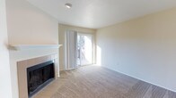This two-floor residence offers a comfortable and functional layout designed for everyday living. The living area serves as the heart of the home, highlighted by a tile-surround fireplace with a classic white mantle that adds a warm, inviting focal point to the room. Soft wall-to-wall carpeting extends throughout the space, contributing to a cozy and comfortable atmosphere underfoot.

Natural light flows generously into the living area through a full-panel sliding glass door, which opens to an outdoor balcony with views of the surrounding environment. The sheer curtains framing the door allow light to diffuse softly throughout the room while maintaining a sense of openness. The walls are finished in a neutral, warm beige tone that complements the light carpeting and creates a clean, airy feel.

The overall design is straightforward and practical, with smooth ceilings and understated architectural details that keep the focus on functionality and livability. The two-floor layout provides a natural separation of living spaces, offering both communal and private areas within the home. The combination of the fireplace, natural light, and access to outdoor space makes this a welcoming residence suited for a variety of lifestyles.