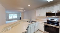 This single-floor residence offers a clean, functional layout with a bright and open feel throughout. The kitchen is a standout feature, equipped with crisp white cabinetry, light countertops, and a full suite of stainless steel appliances including a refrigerator, electric range, and over-the-range microwave. A wraparound peninsula counter connects the kitchen to the living area, creating an open-concept flow ideal for entertaining. Track lighting and recessed fixtures keep the space well-lit.

The bedrooms are generously sized, each finished with plush neutral carpeting and windows that invite natural light and outdoor views of surrounding greenery. Ceiling fans with integrated lighting are featured in the primary bedroom areas, enhancing comfort year-round. A spacious walk-in closet with wire shelving provides ample storage.

Two full bathrooms serve the residence, both finished with tile flooring, white vanity cabinetry, light countertops, and a tub/shower combination. One bathroom features a well-lit vanity mirror with a multi-bulb fixture. A dedicated laundry area houses a stacked washer and dryer unit with additional shelving overhead. The overall palette of warm whites and soft neutrals gives the entire space a clean, move-in-ready ambiance.