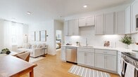 This thoughtfully designed two-bedroom, one-bathroom residence offers a bright and cohesive living experience across a single floor. Light hardwood flooring runs throughout, tying together each room with a warm, consistent aesthetic.

The kitchen is a standout feature, outfitted with gray shaker-style cabinetry, white quartz countertops, a subway tile backsplash, and a full suite of stainless steel appliances including a refrigerator, range, microwave, and dishwasher. Recessed lighting and under-cabinet illumination enhance the space's clean, modern appeal. The kitchen flows naturally into the living area, which benefits from large windows dressed with sheer curtains that invite abundant natural light.

The primary bedroom is a comfortable retreat featuring a ceiling fan, natural light from dual windows, and a dedicated dressing area with dual reach-in closets — ideal for storage and organization. The second bedroom offers flexibility for guests or a home office setup.

The bathroom is finished with a gray vanity, white countertop, and a full tub-shower combination. Hallways connect each area efficiently, contributing to the unit's practical and navigable layout. Overall, the residence presents a clean, contemporary design with functional details throughout.